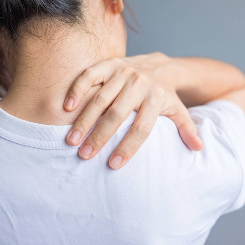 A person in a white shirt holds their shoulder and neck, suggesting upper back pain; natural relief may help.