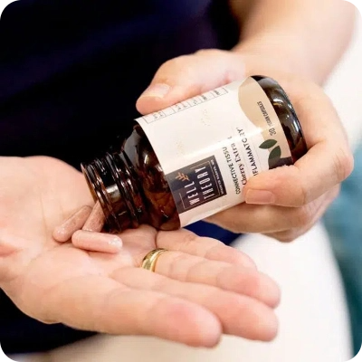 A person pours supplements from a brown bottle into their hand, wearing a gold ring on one finger.