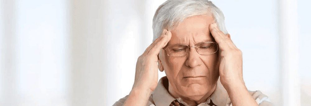 Older man with gray hair and glasses holds his temples, eyes closed, appearing to seek natural pain relief.