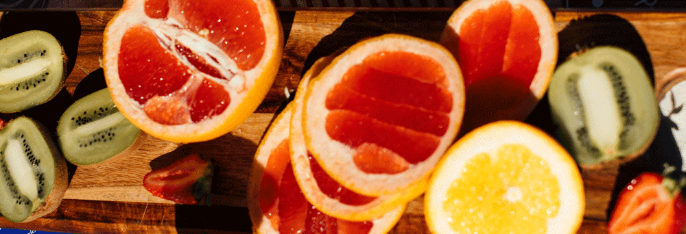 Sliced grapefruit, kiwi, and orange on a wooden cutting board under bright light.