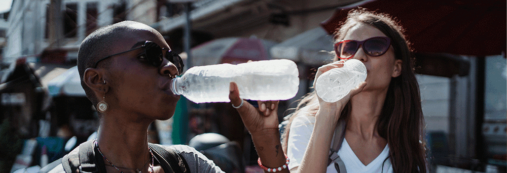 Two people outdoors in sunglasses enjoy water bottles on a sunny day, chatting about wellness and supplements.