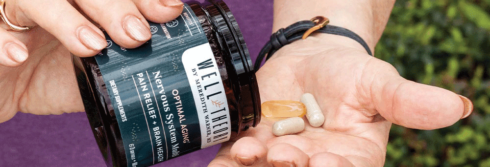 A hand holds supplements beside a jar labeled “WELL THEORY Nervous System, Pain Relief, Brain Health.”.