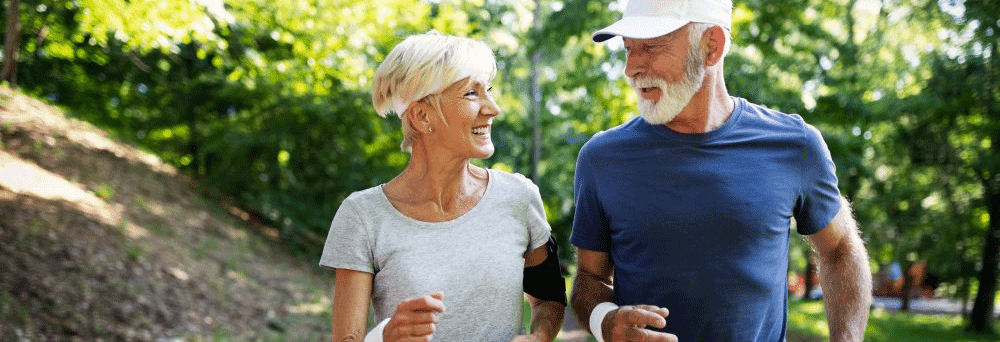 Two older adults smiling and jogging outdoors in athletic wear, enjoying an active lifestyle supported by supplements.