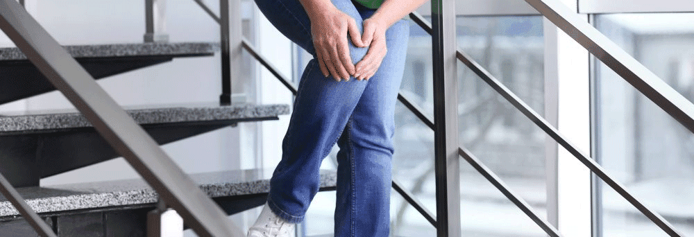 Person on stairs holding their knee in pain, suggesting they may benefit from natural surgeon-formulated supplements.