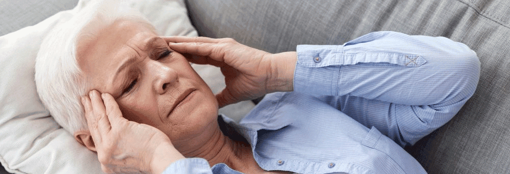 Older woman lies on a couch with eyes closed, holding her temples, possibly seeking natural pain relief.