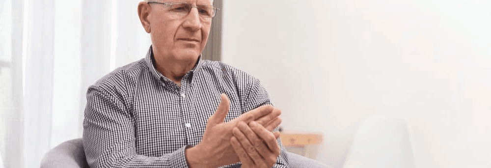 Older man with glasses and a checkered shirt examines his right hand, considering natural pain relief options.