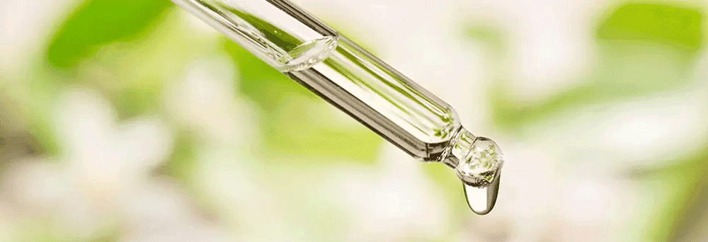 Close-up of a glass dropper with a liquid drop and surgeon-formulated supplements, against a blurred green background.