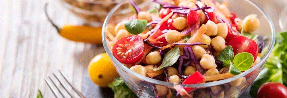 Glass bowl with a colorful salad of chickpeas, cherry tomatoes, red cabbage, and basil next to supplements.