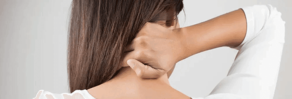Person with long brown hair touches their neck, wearing a white top, as seen in natural pain relief ads.