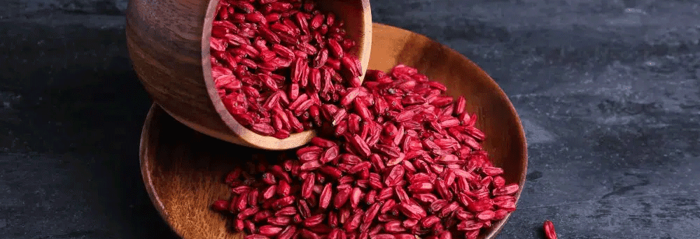 Red rice grains spill from a wooden bowl onto a dark textured surface, highlighting their natural appeal.