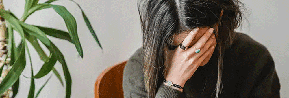 A person sits with their head in their hand beside a green leafy plant, suggesting natural supplement benefits.