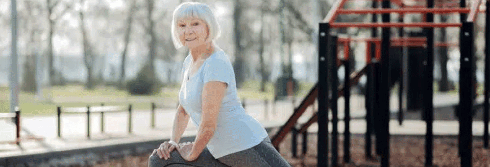 Older woman in athletic wear stretches on a park bench, promoting natural pain relief supplements outdoors.