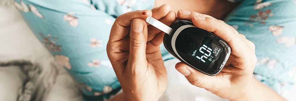 Person in blue pajamas checks blood sugar with a glucometer, suggesting daily wellness through natural supplements.