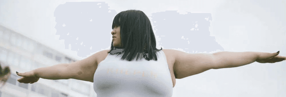 A person with straight black hair stands outdoors, arms outstretched, radiating wellness and vitality.