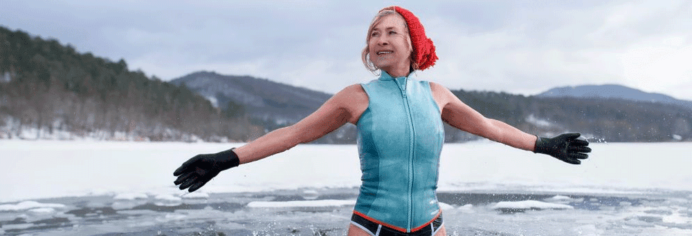 A woman in a sleeveless bodysuit, red hat, and gloves stands waist-deep in an icy lake, embracing nature.