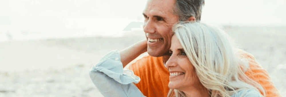 A smiling older couple sits together on a calm beach, chatting about natural pain relief supplements.