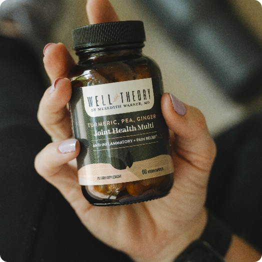 A hand holds a bottle of Well Theory Turmeric, Pea, Ginger Joint Health supplement with 60 capsules.