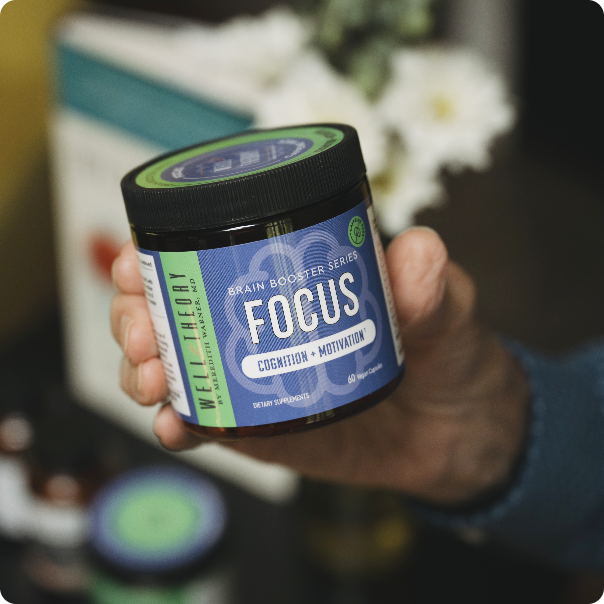 A person holds a "FOCUS" brain booster jar, with flowers blurred in the background.