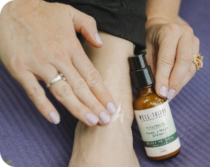 A person applies "HEEL THERAPY" cream to their ankle, the tube resting on a purple surface.