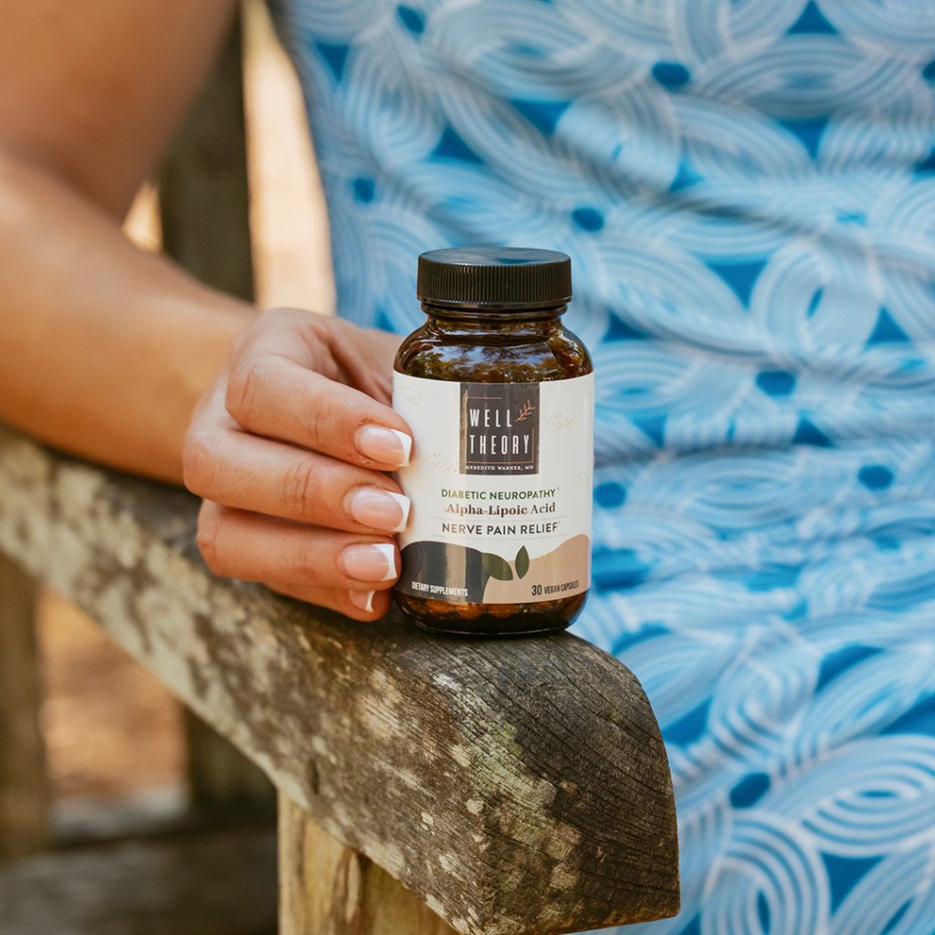 A person in a blue dress sits on a wooden bench holding a bottle of supplements for nerve pain.