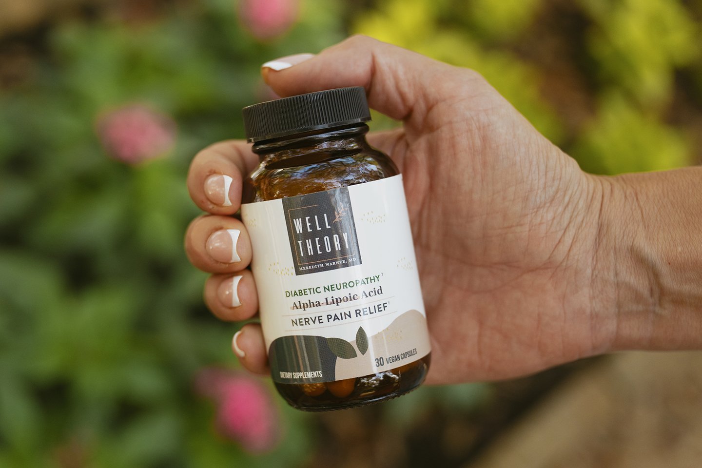 A hand holds a "Well Theory Diabetic Neuropathy Alpha Lipoic Acid Nerve Pain Relief" supplement bottle outdoors.