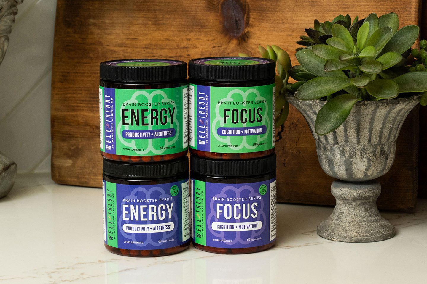 Four “Energy” and “Focus” Brain Booster supplement jars next to a potted succulent on a kitchen counter.