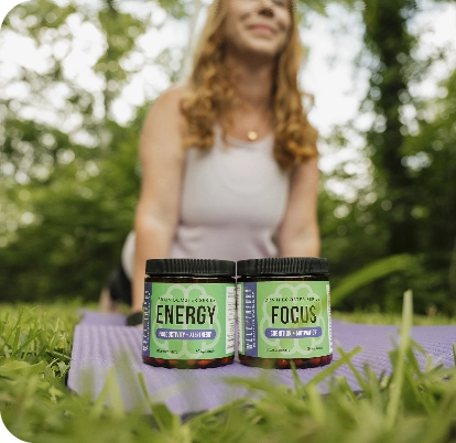 A woman practices yoga outdoors with "Energy" and "Focus" gummies on the grass in the foreground.