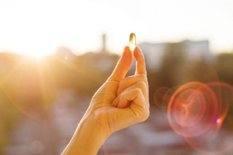 A hand holds a translucent capsule against sunlight, emphasizing surgeon-formulated natural supplements.