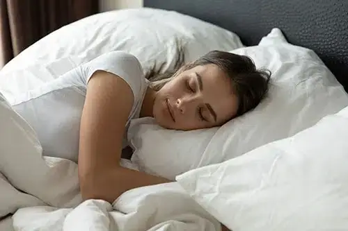 A person with long hair sleeps on their side in white sheets after taking natural pain relief supplements.