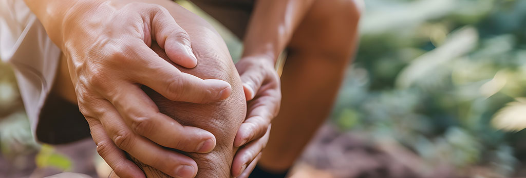 Close-up of a person holding their knee in discomfort outdoors, suggesting need for natural pain relief.