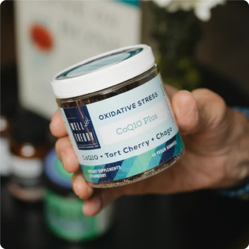 A hand holds a jar of "Oxidative Stress CoQ10 Plus Tart Cherry + Chaga" by Well Theory.